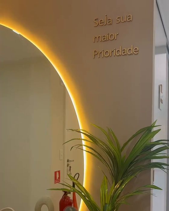 Recepção com espelho em arco retroiluminado e a frase “Seja sua maior prioridade” aplicada na parede.