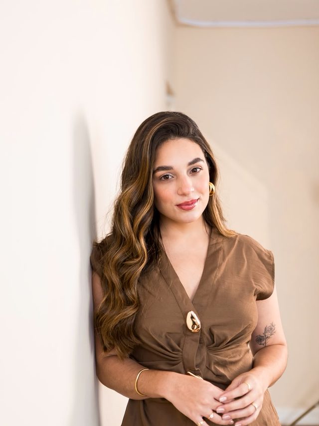 Dra. Luíse Ferrão, biomédica esteta, em retrato encostada em uma parede clara.