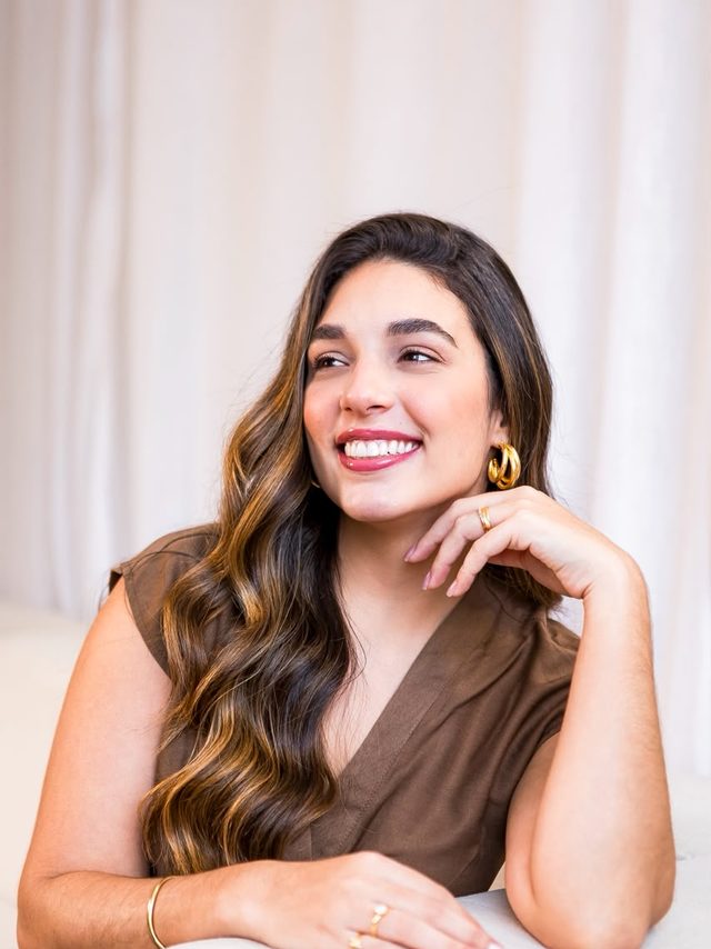 Dra. Luíse Ferrão sorrindo, sentada em ambiente claro da clínica.