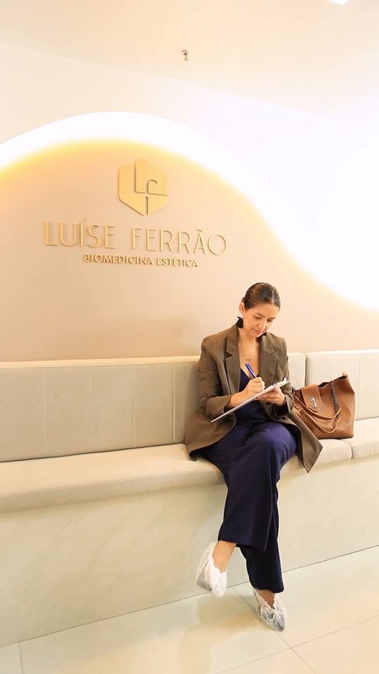 Recepção da clínica, com paciente sendo atendida sob a parede curva iluminada com o logotipo dourado.